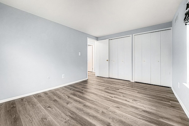 unfurnished bedroom with visible vents, baseboards, multiple closets, and wood finished floors