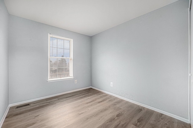 spare room with wood finished floors, visible vents, and baseboards