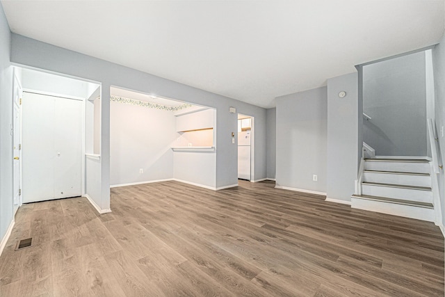 unfurnished living room with stairway, baseboards, visible vents, and wood finished floors