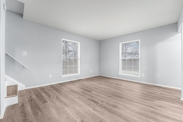 empty room with baseboards, stairs, and light wood finished floors