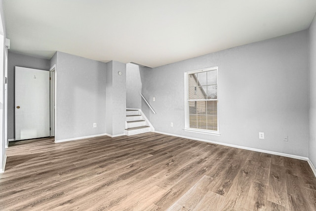 unfurnished living room with stairs, baseboards, and wood finished floors