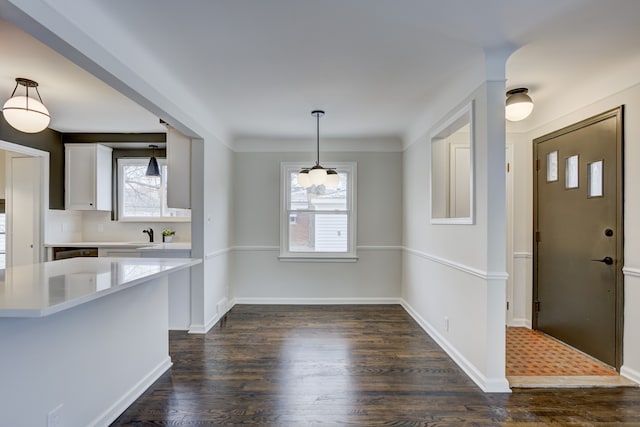 unfurnished dining area featuring dark wood finished floors, baseboards, and a sink