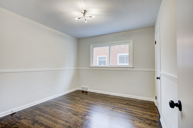 empty room with dark wood-style floors, visible vents, and baseboards