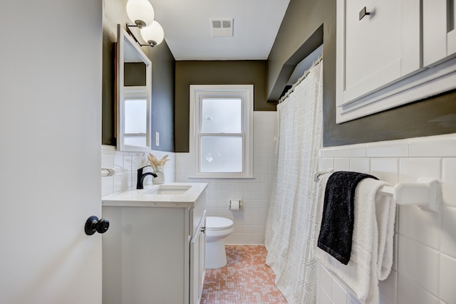 full bath with visible vents, toilet, tile walls, wainscoting, and vanity