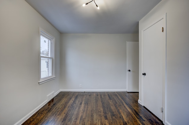 spare room featuring baseboards and dark wood-type flooring