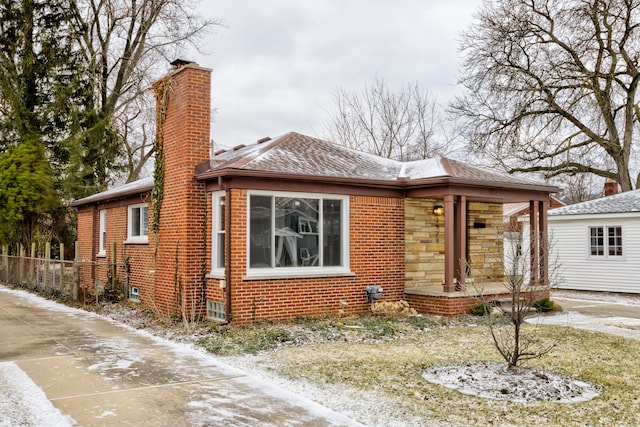 bungalow featuring stone siding, a porch, fence, brick siding, and a chimney