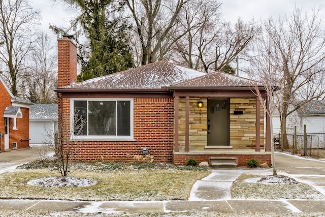 bungalow-style house with stone siding, brick siding, covered porch, and a chimney