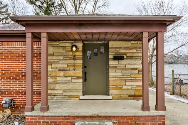 view of exterior entry with brick siding, stone siding, and fence