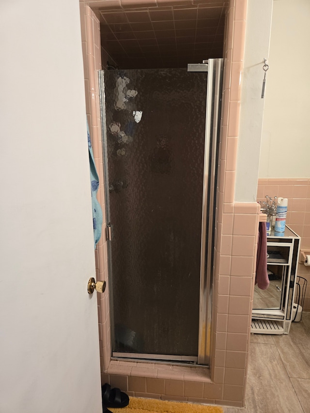 full bathroom featuring a wainscoted wall, a stall shower, and tile walls