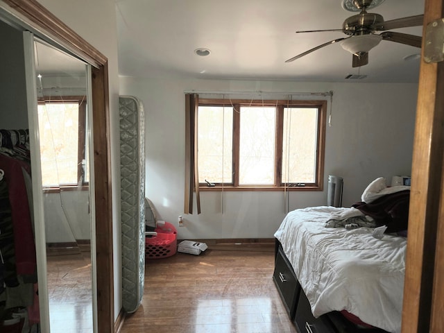 bedroom with a ceiling fan, wood finished floors, visible vents, and baseboards