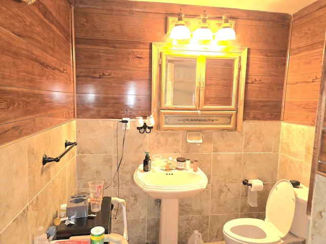 bathroom featuring toilet, tile walls, and a sink