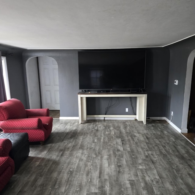 living area with wood finished floors, arched walkways, and baseboards