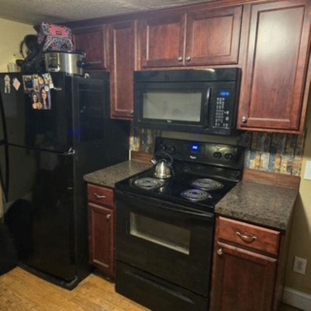 kitchen with a textured ceiling, black appliances, and light wood finished floors