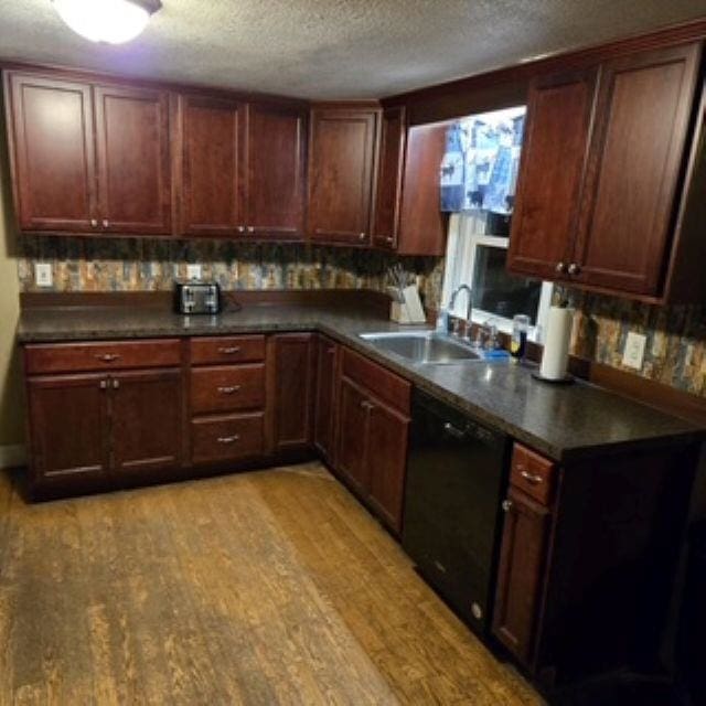 kitchen featuring a sink, black dishwasher, dark countertops, and light wood-style flooring