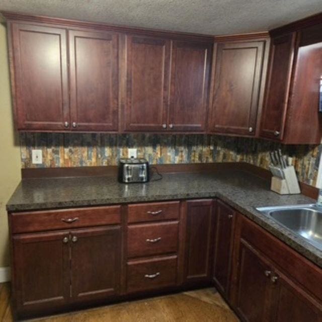 kitchen featuring a sink, dark stone countertops, light wood-style floors, and a textured ceiling