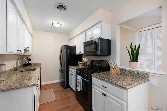 kitchen featuring visible vents, light wood-style flooring, white cabinets, black appliances, and a sink