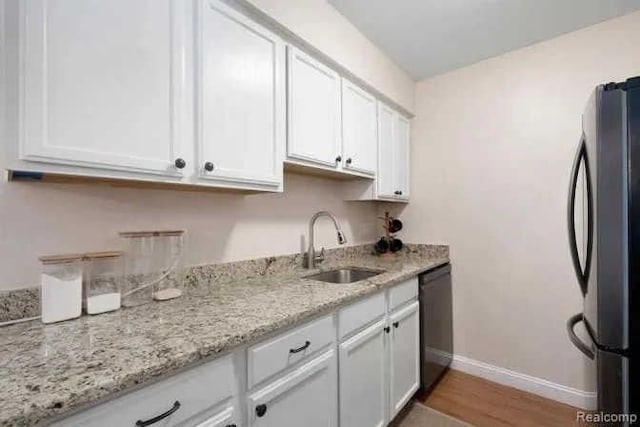 kitchen with a sink, black dishwasher, freestanding refrigerator, white cabinets, and baseboards