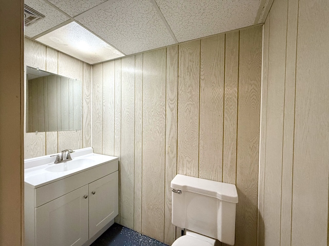 half bath with a drop ceiling, wood walls, and vanity