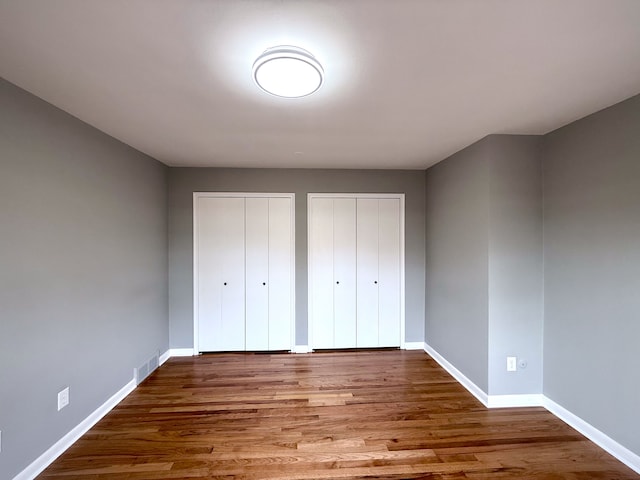 unfurnished bedroom featuring visible vents, wood finished floors, baseboards, and two closets