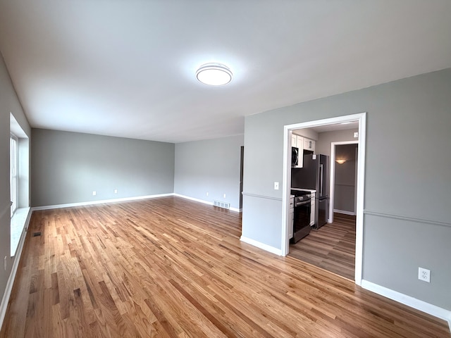 empty room with light wood-style flooring, visible vents, and baseboards