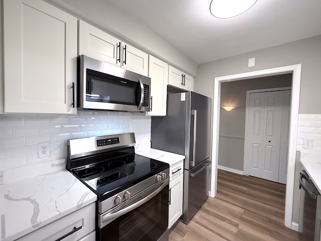 kitchen with white cabinetry, stainless steel appliances, light wood-style floors, and light stone countertops