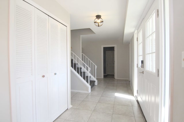 foyer entrance with light tile patterned floors, stairs, and baseboards