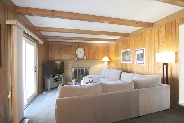 living room featuring beam ceiling, wooden walls, a brick fireplace, and light carpet