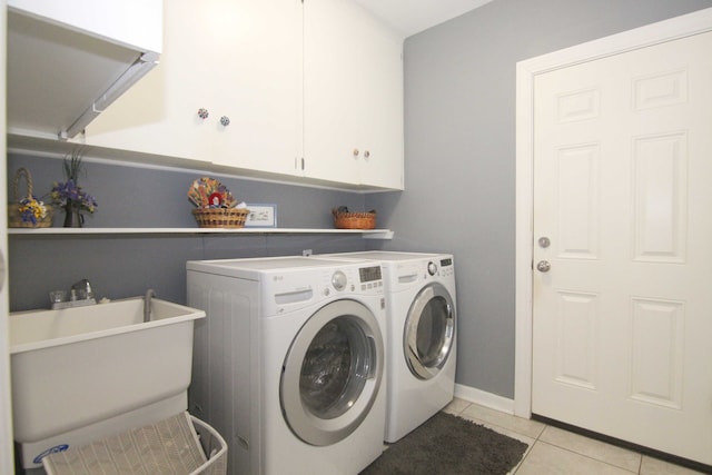 clothes washing area with a sink, washing machine and dryer, cabinet space, light tile patterned floors, and baseboards