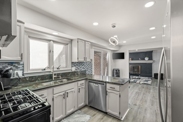 kitchen with a peninsula, a sink, light wood-style floors, appliances with stainless steel finishes, and tasteful backsplash