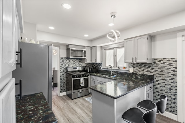 kitchen with a sink, light wood-style floors, appliances with stainless steel finishes, and a peninsula