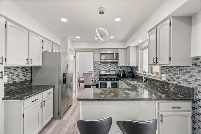 kitchen featuring a sink, a peninsula, dark stone countertops, and stainless steel appliances