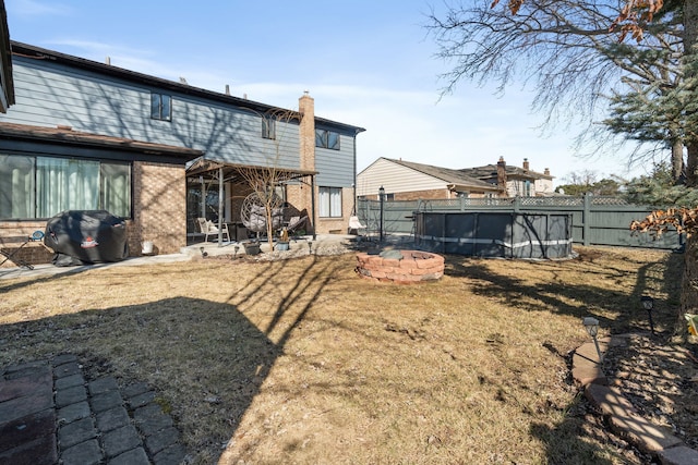 rear view of property featuring a fenced in pool, brick siding, a fenced backyard, and an outdoor fire pit