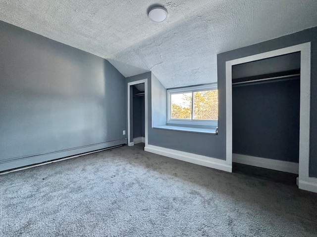 unfurnished bedroom featuring two closets, a baseboard heating unit, baseboards, carpet, and vaulted ceiling