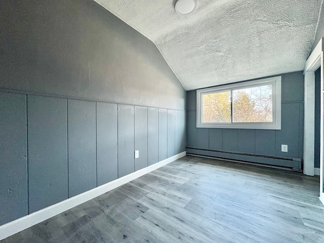 spare room with a textured ceiling, wood finished floors, lofted ceiling, wainscoting, and baseboard heating