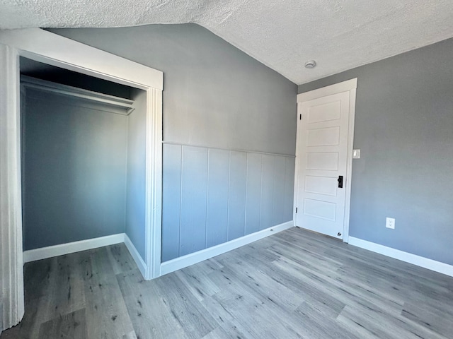 unfurnished bedroom with a closet, a textured ceiling, wood finished floors, and vaulted ceiling