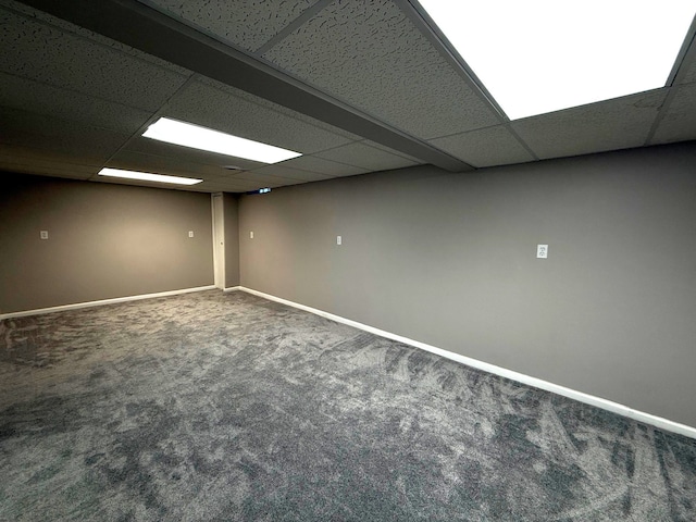 finished below grade area featuring a drop ceiling, baseboards, and carpet floors