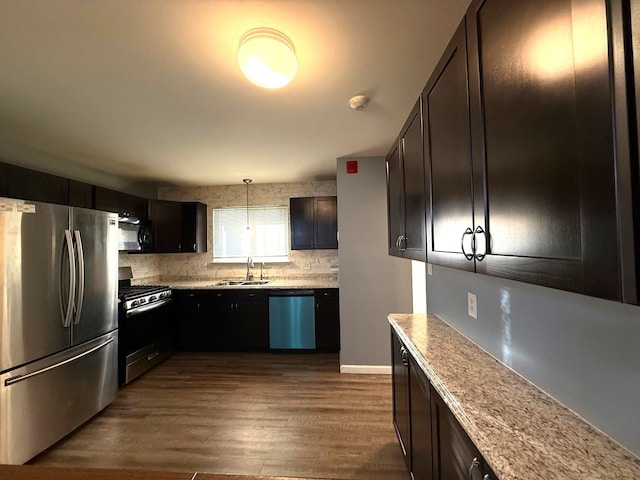 kitchen featuring light stone countertops, dark wood-style floors, a sink, stainless steel appliances, and backsplash