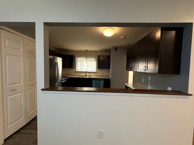 kitchen featuring dark countertops, backsplash, dark wood-type flooring, stainless steel appliances, and a sink