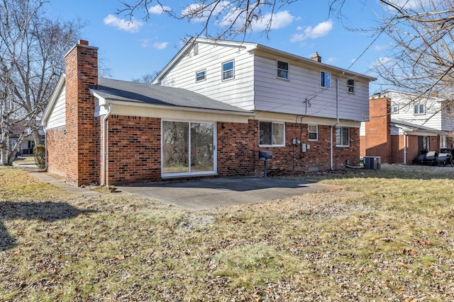 back of house with brick siding, a yard, a chimney, and a patio