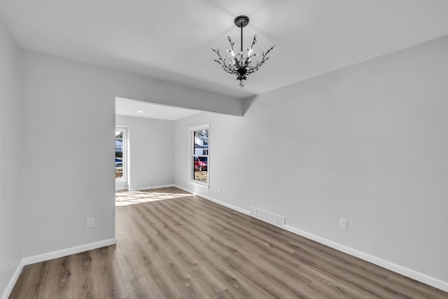 empty room featuring a notable chandelier, visible vents, baseboards, and wood finished floors