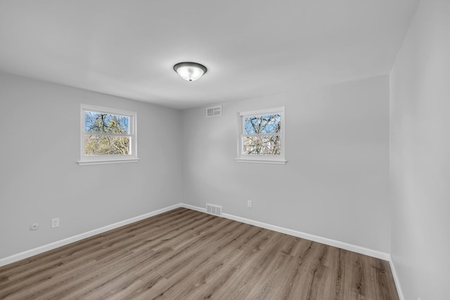 spare room with visible vents, plenty of natural light, baseboards, and wood finished floors