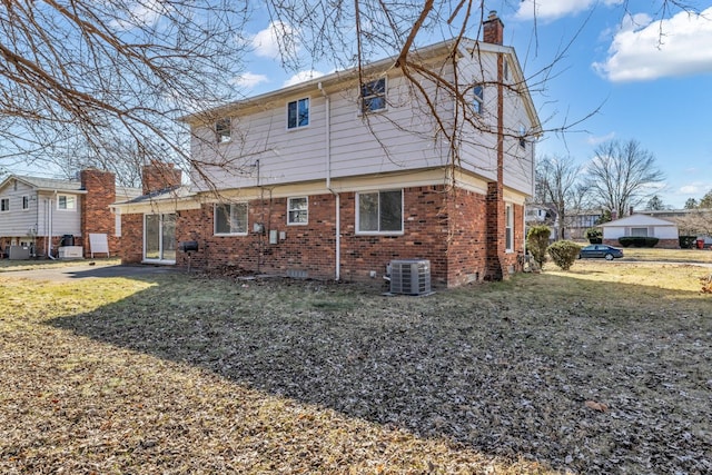 rear view of property with brick siding, a lawn, cooling unit, and a chimney