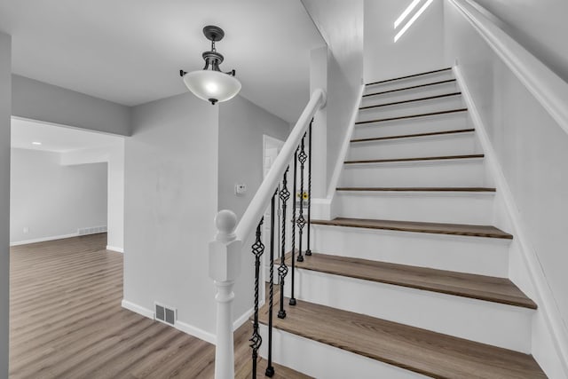 staircase with wood finished floors, visible vents, and baseboards