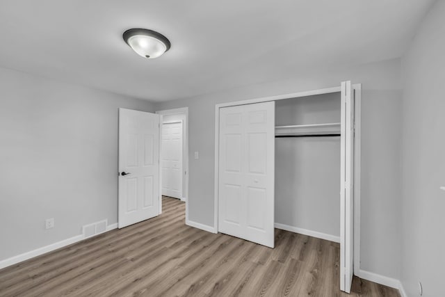 unfurnished bedroom with visible vents, baseboards, a closet, and wood finished floors