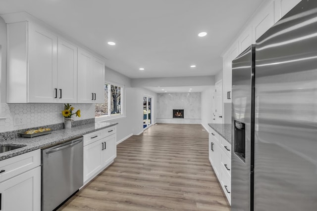 kitchen featuring backsplash, open floor plan, light wood-style floors, white cabinets, and stainless steel appliances