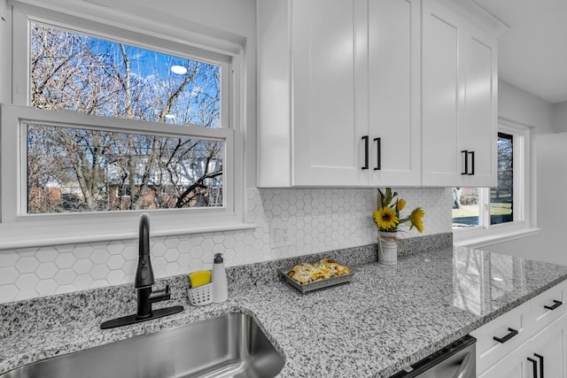 kitchen featuring a sink, light stone counters, backsplash, stainless steel dishwasher, and white cabinetry