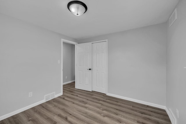 unfurnished bedroom featuring a closet, visible vents, baseboards, and wood finished floors