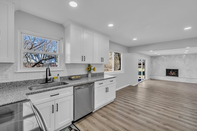 kitchen with light wood finished floors, a fireplace, a sink, stainless steel dishwasher, and open floor plan