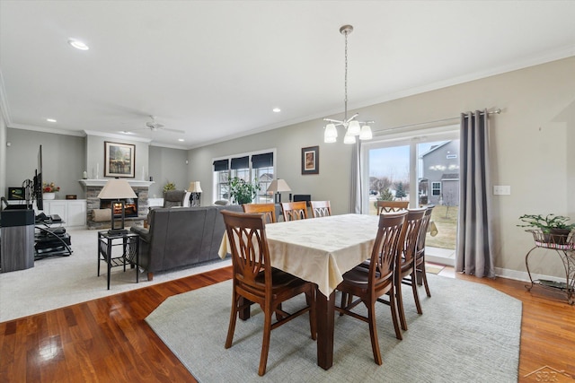 dining room featuring wood finished floors, baseboards, recessed lighting, a fireplace, and crown molding