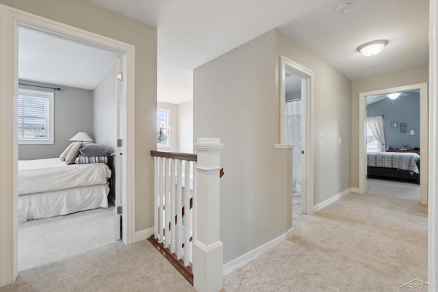 hall with baseboards, an upstairs landing, and carpet floors